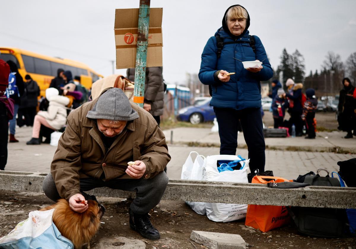 Un hombre da de comer a su perro en el control fronterizo de Medyka, en Polonia, tras huir de Ucrania.