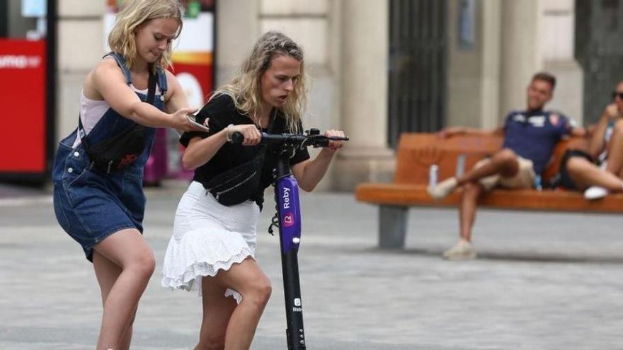 Dos jóvenes intentan subirse a un patinete compartido en Barcelona, en agosto de 2019, cuando las empresas operaban sin paraguas legal.