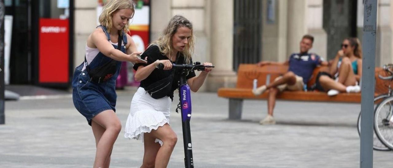 Dos jóvenes intentan subirse a un patinete compartido en Barcelona, en agosto de 2019, cuando las empresas operaban sin paraguas legal.