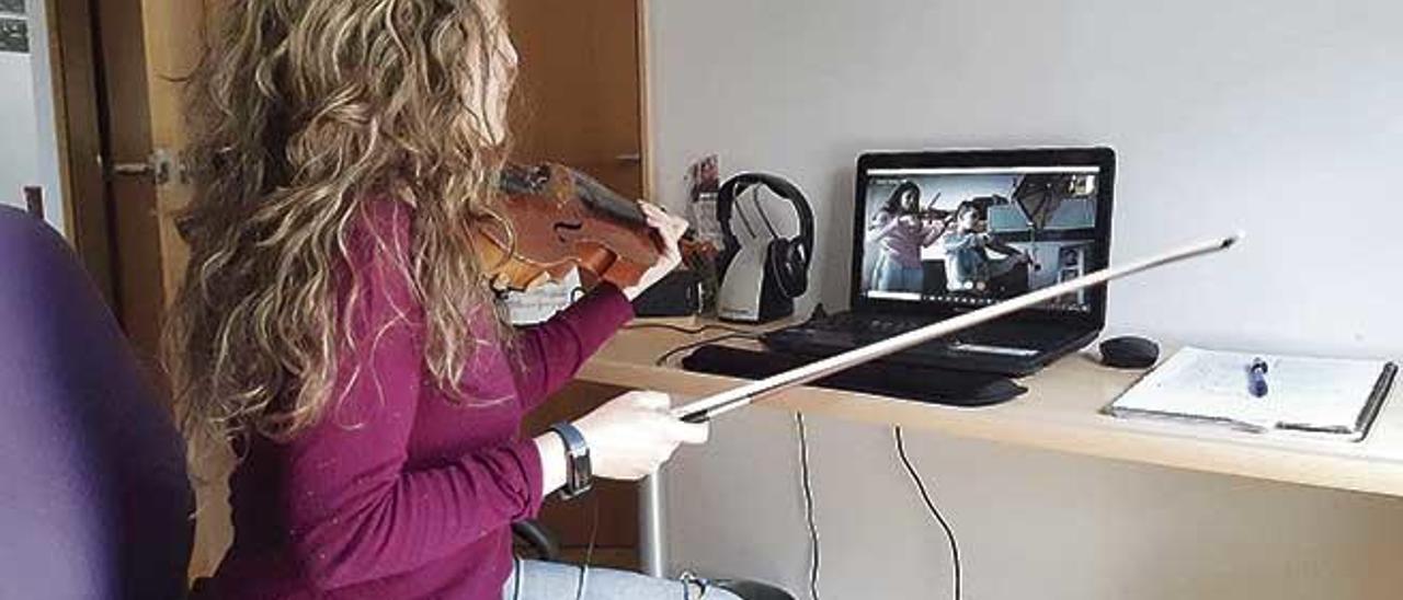 Una joven practica con su violín a través de un chat con su profesor durante el confinamiento.