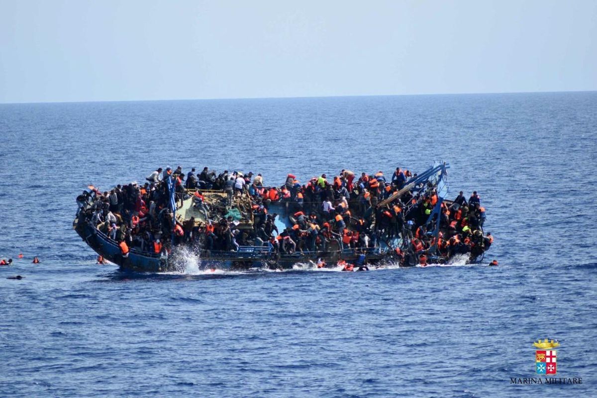 El barco, lleno de inmigrantes, se ladea y comienza a caer gente al agua.