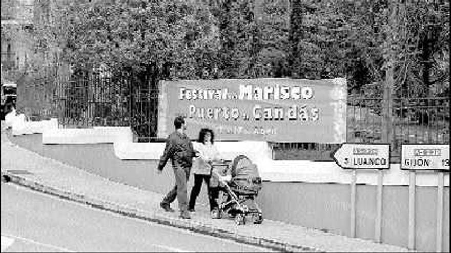 Dos turistas, delante de uno de los carteles que anuncian las II Jornadas gastronómicas del marisco y la sidra de Candás.