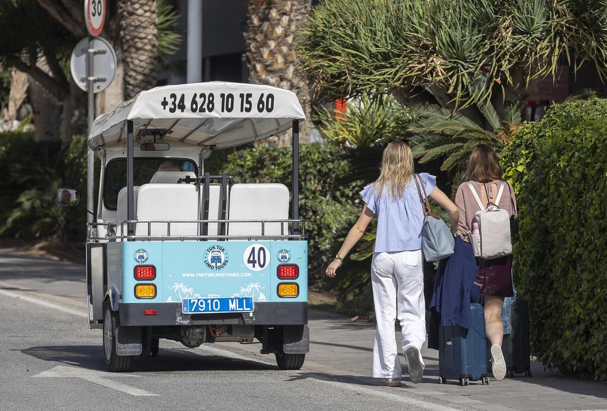 Dos turistas pasan con maletas junto a un tuk tuk estacionado en una zona de hoteles en Alicante, esta semana.