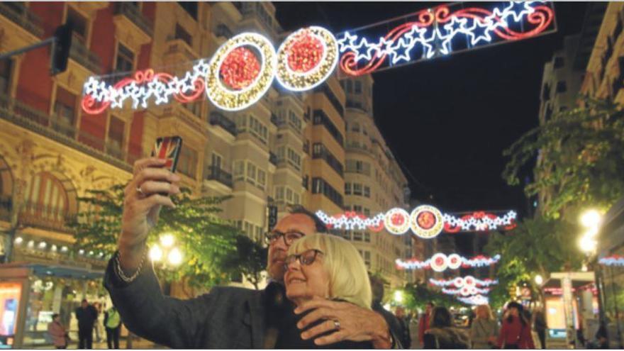 Una pareja se hace una foto en la Rambla de Alicante con las luces navideñas detrás.