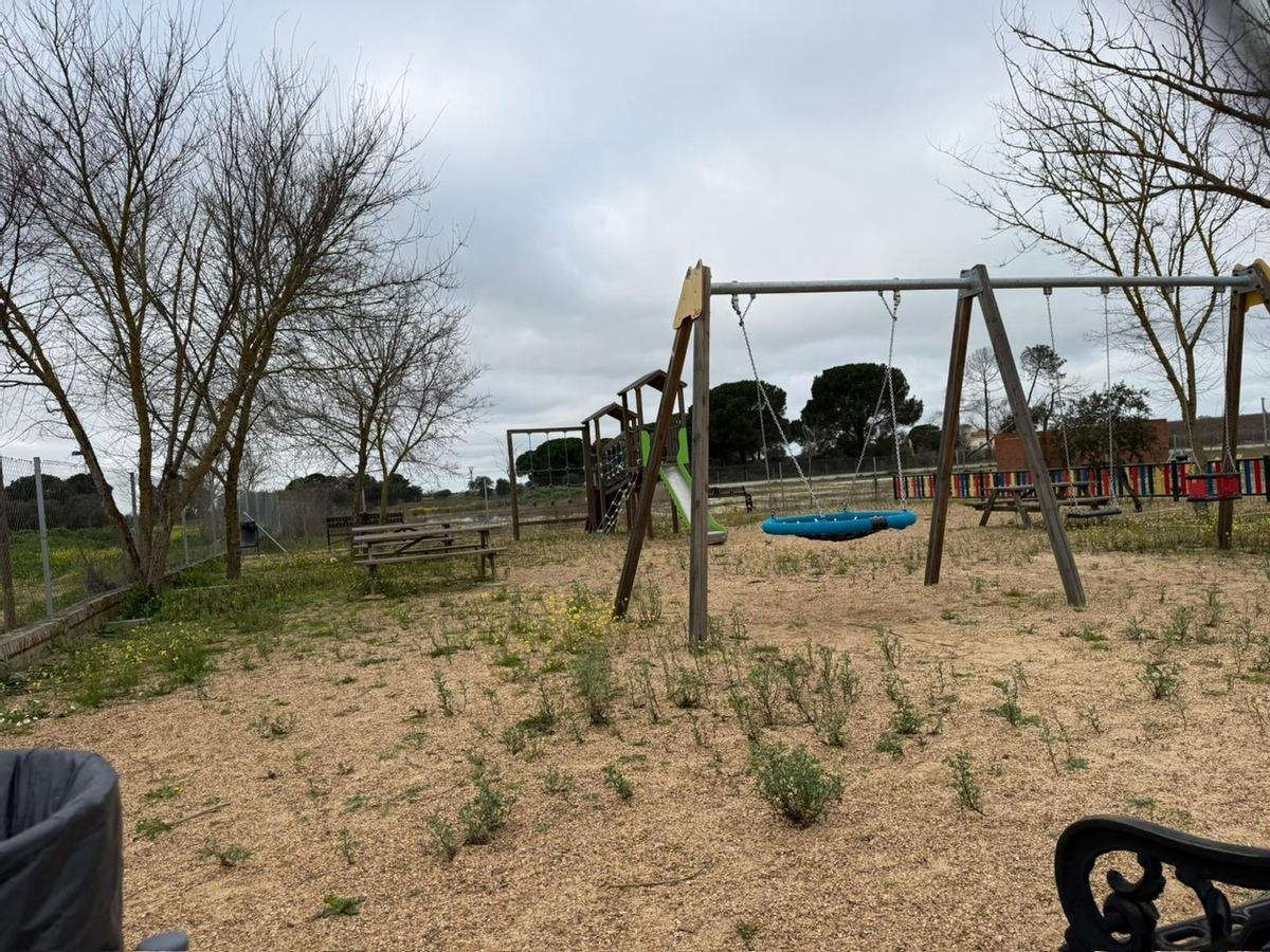 Parque infantil de la pedanía Alcazaba (Badajoz) con malas hierbas en la zona de juegos.