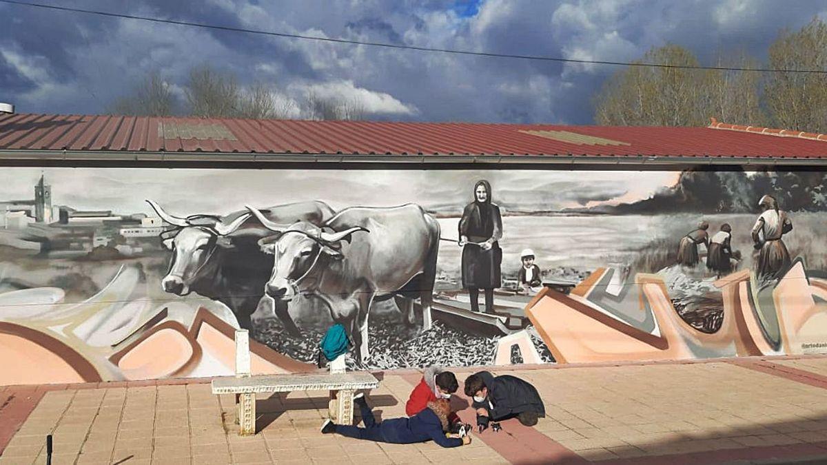 Tres niños juegan ante el mural sobre la mujer rural pintado en Villaescusa.