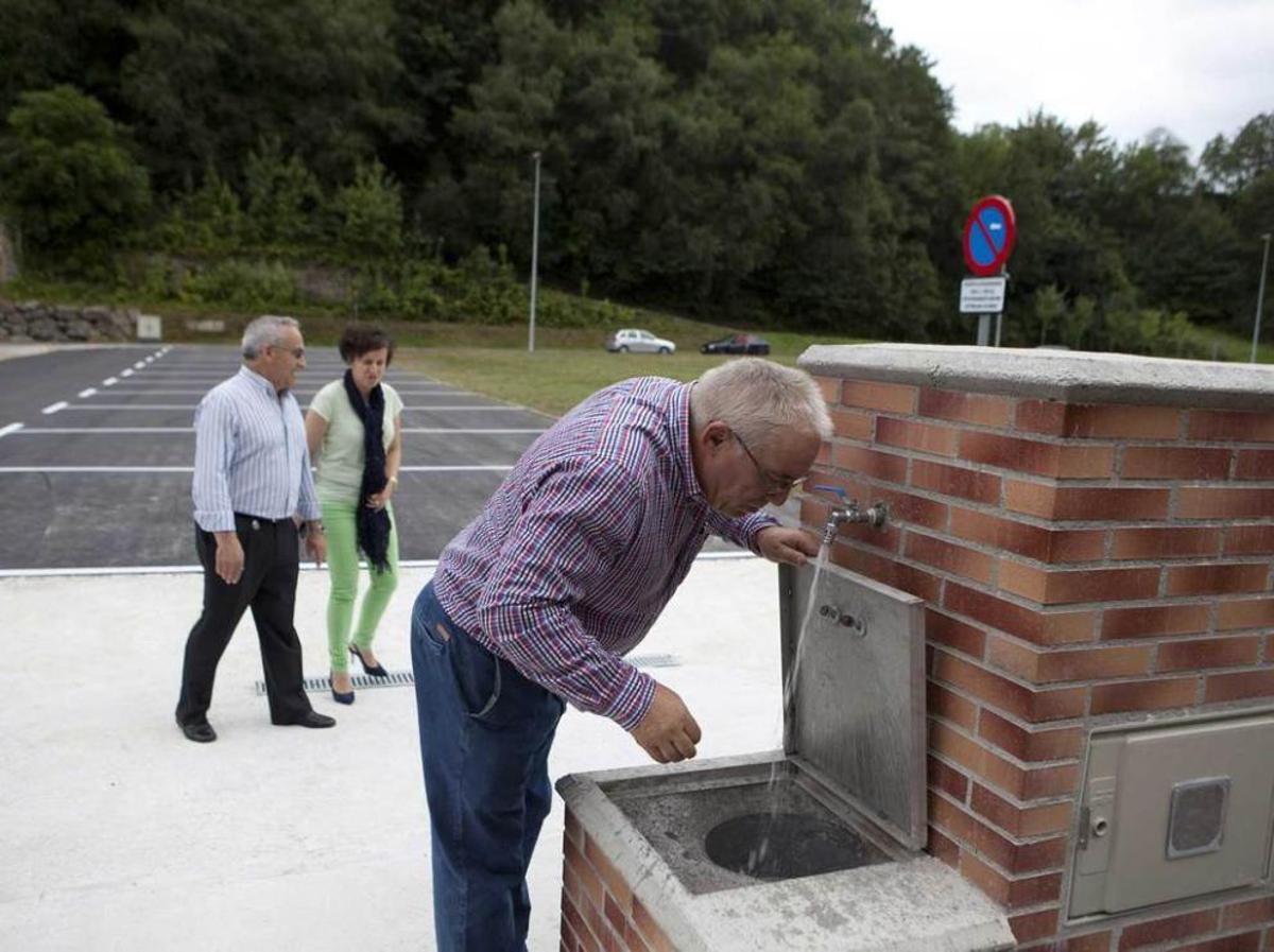 El edil José Manuel Álvarez bebe agua en el área de autocaravanas, con María y Vicente Fernández detrás.