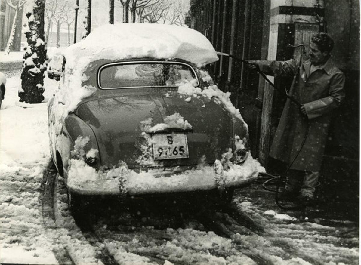 Un barcelonés, manguera en mano, trata de disolver la nieve del techo de su coche.