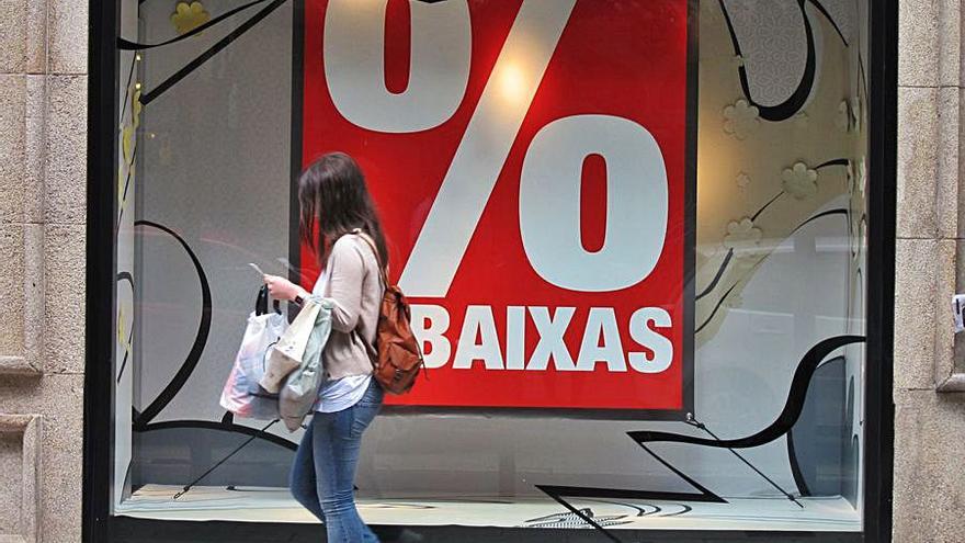 Una joven camina ante un cartel de rebajas en Galicia