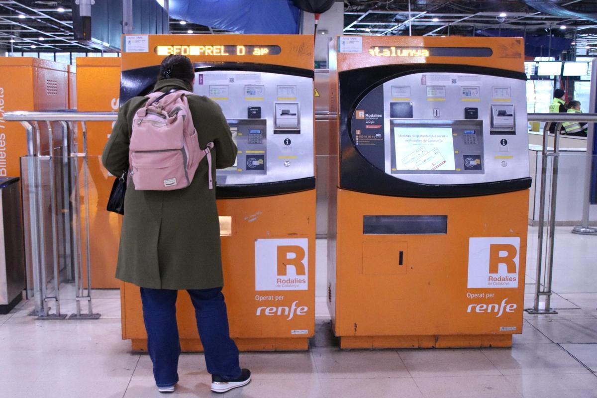 Una persona adquirint un bitllet a les màquines de venda de Rodalies