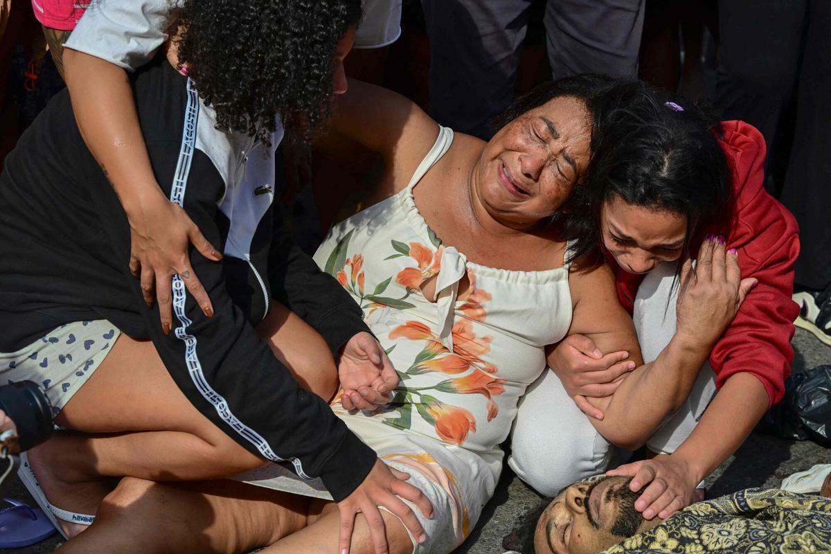 EDITORS NOTE: Graphic content / TOPSHOT - Women weep next to a dead man lying among a line of bodies on Sao Lucas Square of the Vila Cruzeiro favela at the Penha complex in Rio de Janeiro, Brazil, on October 29, 2025, in the aftermath of Operacao Contencao (Operation Containment). Residents of a favela in Rio de Janeiro lined up more than 40 bodies at a plaza in their low-income neighborhood on Ocotber 29, a day after the bloodiest police operation in the citys history, AFP reported. (Photo by Pablo PORCIUNCULA / AFP). Graphic content