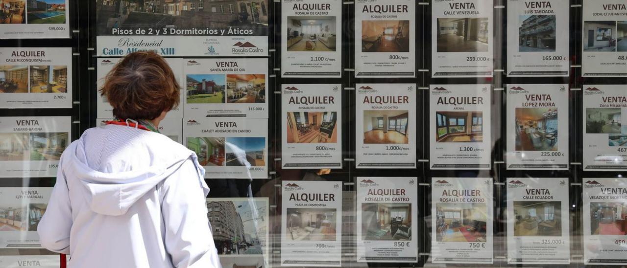 Una mujer ve anuncios de pisos en el escaparate de una inmobiliaria de Vigo.