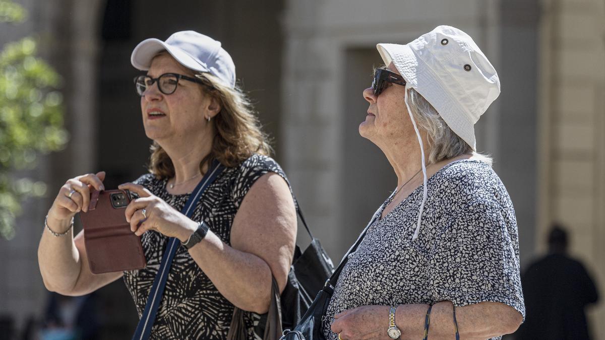 Dos mujeres con ropa veraniega se protegen con gorra y sombrero la cabeza del sol.