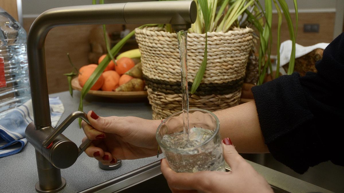 Una mujer abre el grifo para llenar un vaso de agua.
