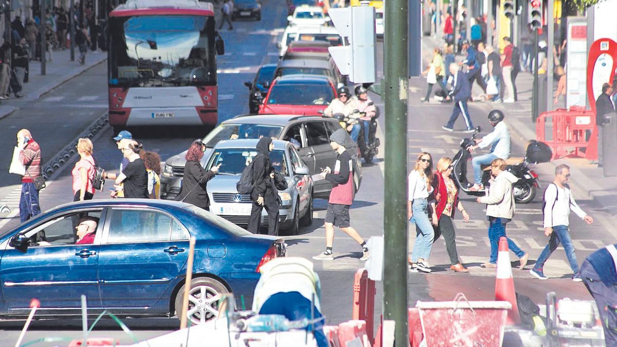 Numerosas personas cruzan la Gran Vía de Murcia con decenas de vehículos circulando por la calzada.