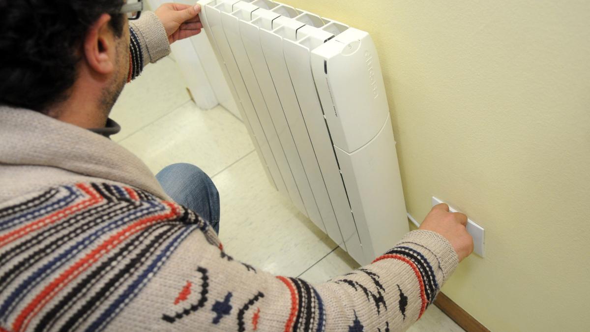 Un hombre enchufa un radiador eléctrico.