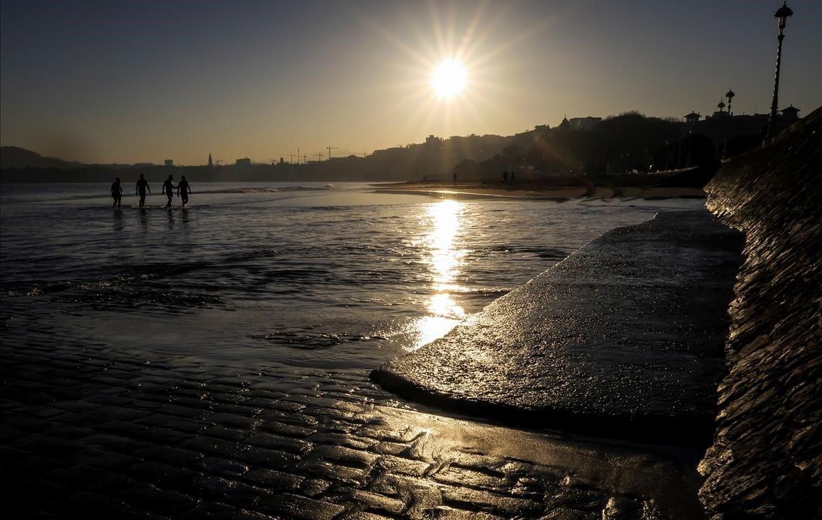 Varios hombres salen del agua, al amanecer, en la playa de Ondarreta de San Sebastián.