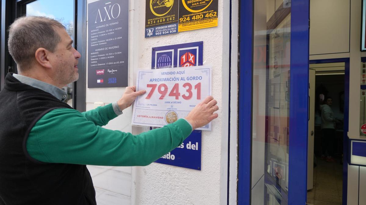 José Miguel Guijarro, responsable de la administración La Paloma de Badajoz, coloca el cartel que acredita que ha vendido la aproximación al Gordo 2025.