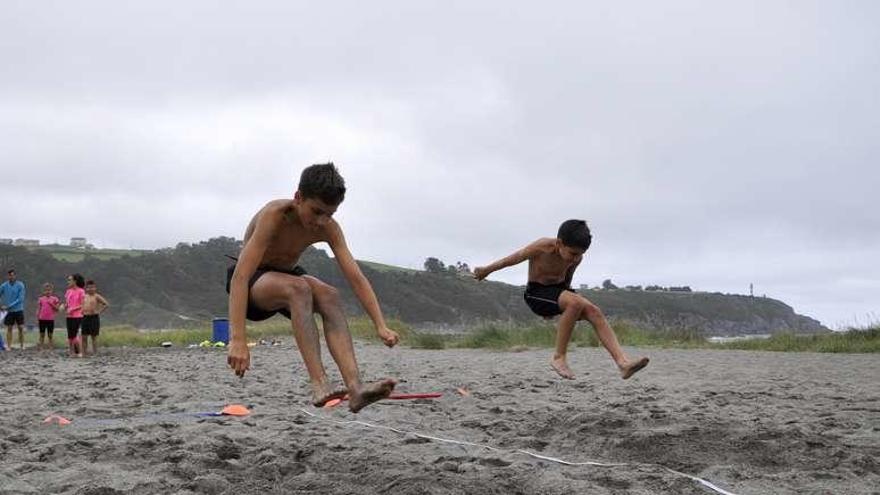 Arriba, dos niños, durante el salto de longitud en la playa de Navia. A la izquierda, en uno de los juegos.