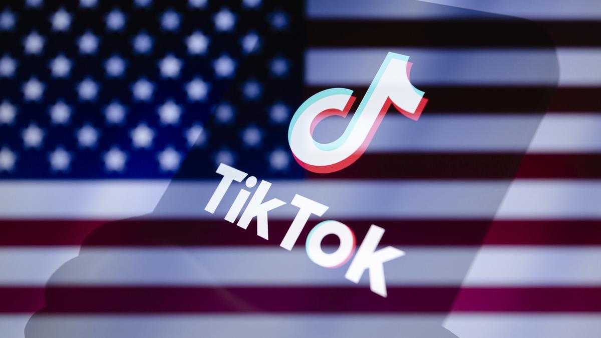 Logo de Tiktok en un móvil, con la bandera de Estados Unidos al fondo.