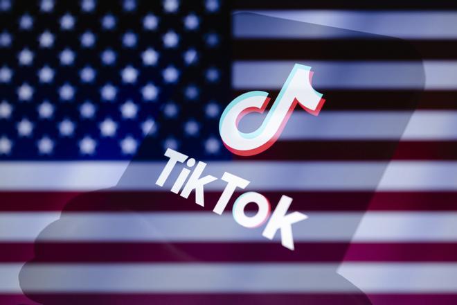 Logo de Tiktok en un móvil, con la bandera de Estados Unidos al fondo.