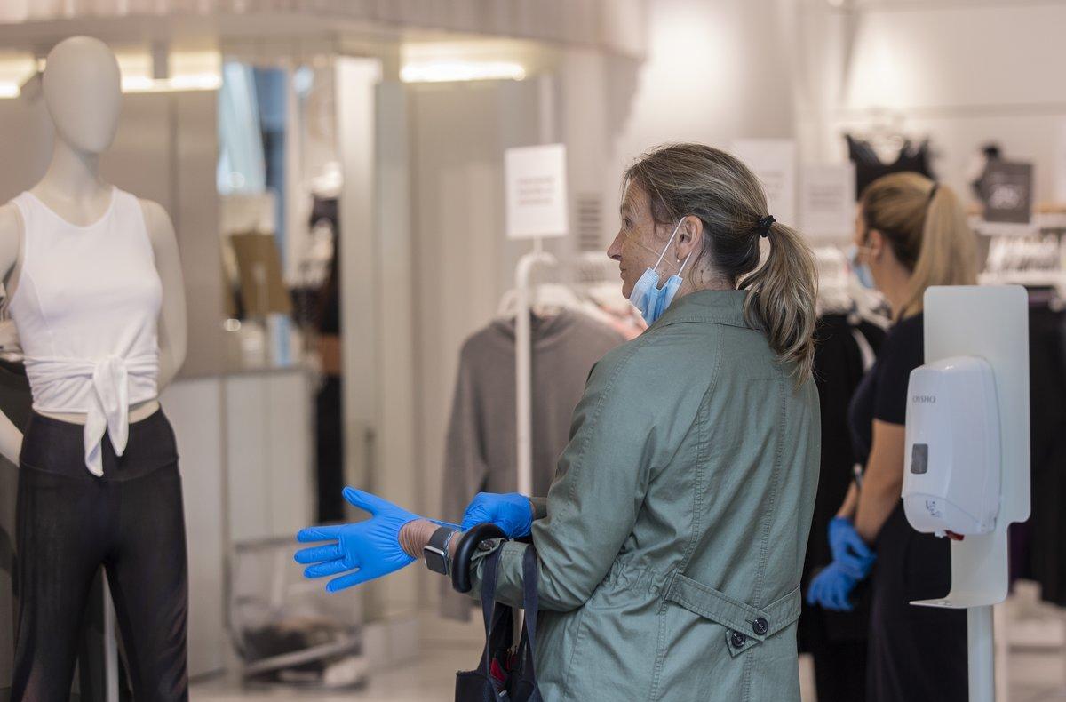 Una mujer se coloca unos guantes proporcionados por el establecimiento al entrar en una tienda de ropa. durante el segundo dÃ­a de la fase 1 del plan de desescalada que ha elaborado el Gobierno de EspaÃ±a. En Sevilla, (AndalucÃ­a, EspaÃ±a), a 12 de mayo de 2020.