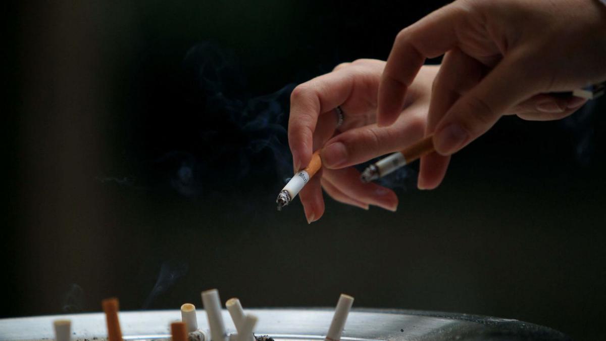 Dos fumadores tiran la ceniza de su cigarrillo en un cenicero.   | // MARCELO SAYÃO