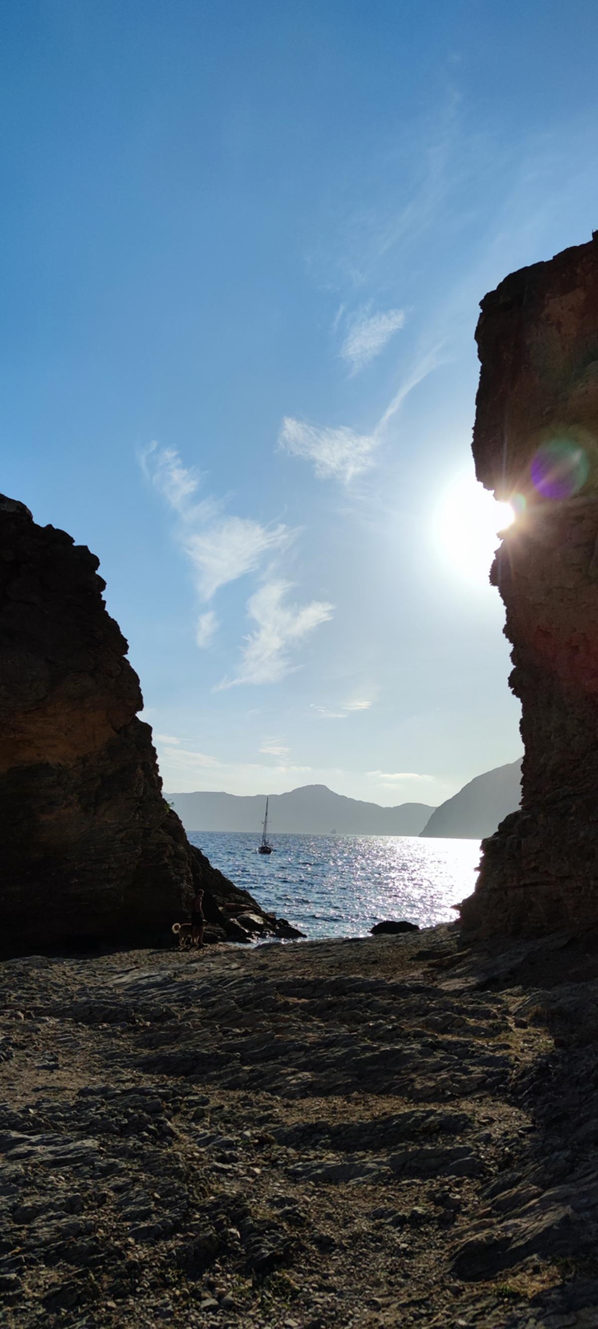 Playa de arena oscura y acantilados. Bahía en España con un yate