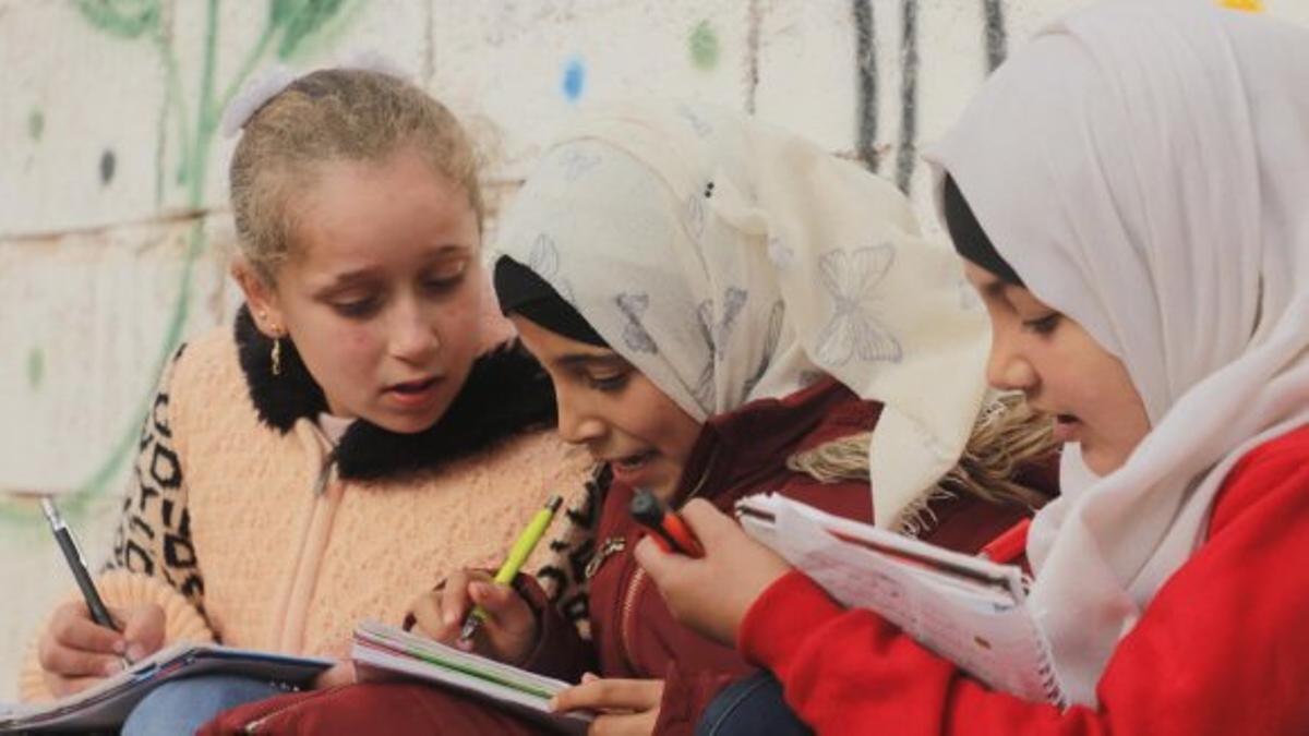 Tres niñas sirias dibujan en el recreo de un colegio.