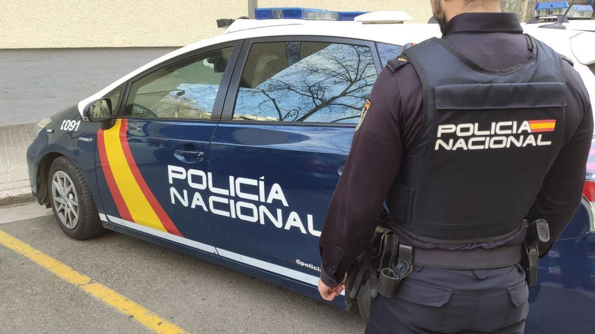 Un agente de la Policía Nacional junto a un coche patrulla.