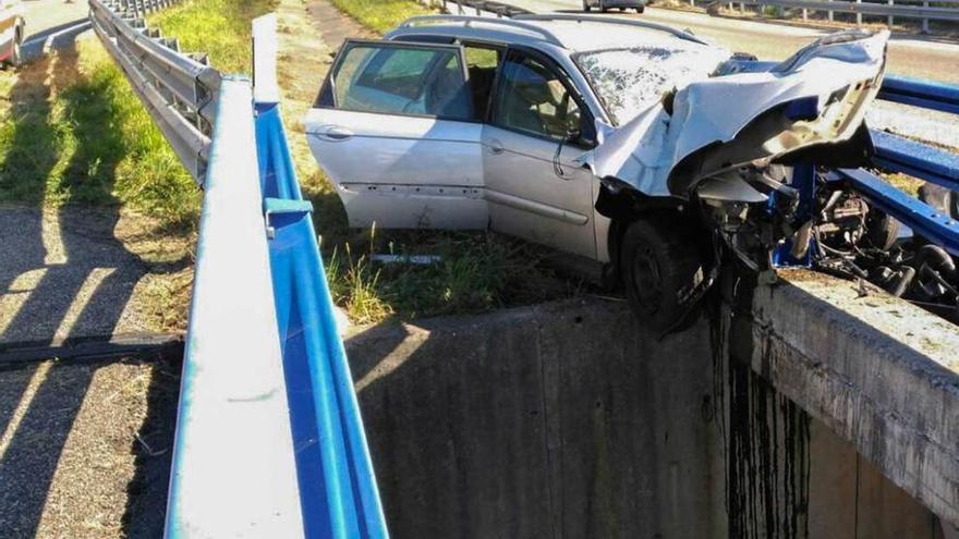 El coche implicado en el accidente, a punto de caer por el viaducto.