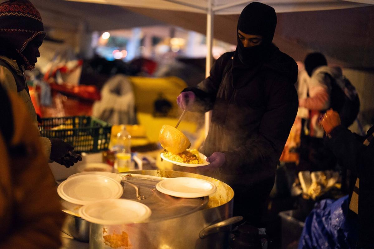 Voluntarios de distintas entidades privadas reparten comida para la cena de Nochebuena bajo la autopista C-31, donde aún duermen decenas de personas desalojadas del antiguo instituto B9