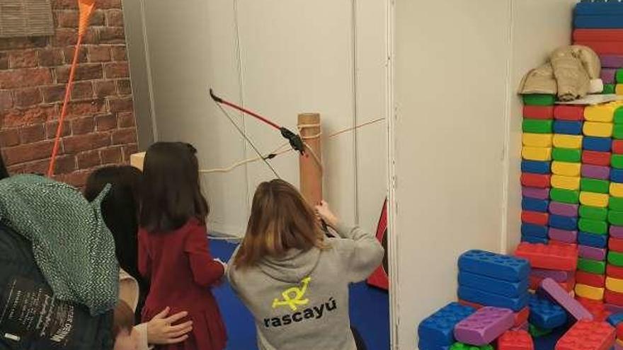 Dos niñas realizan tiro con arco junto a una monitora.