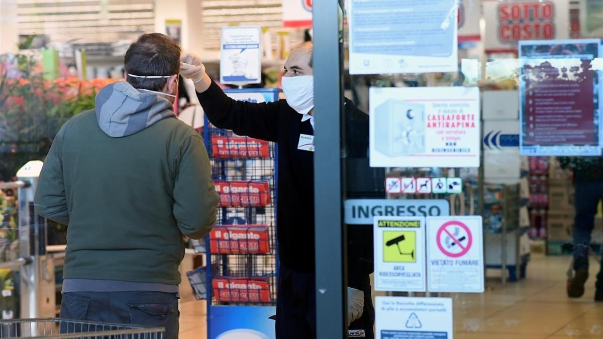 Un empleado de un supermercado toma la temperatura de un cliente a la entrada del establecimiento, el lunes en Milán.