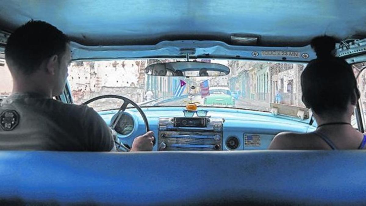 Un taxista en su vehículo de los años 50 con las banderas de Cuba y EEUU avanza por La Habana.