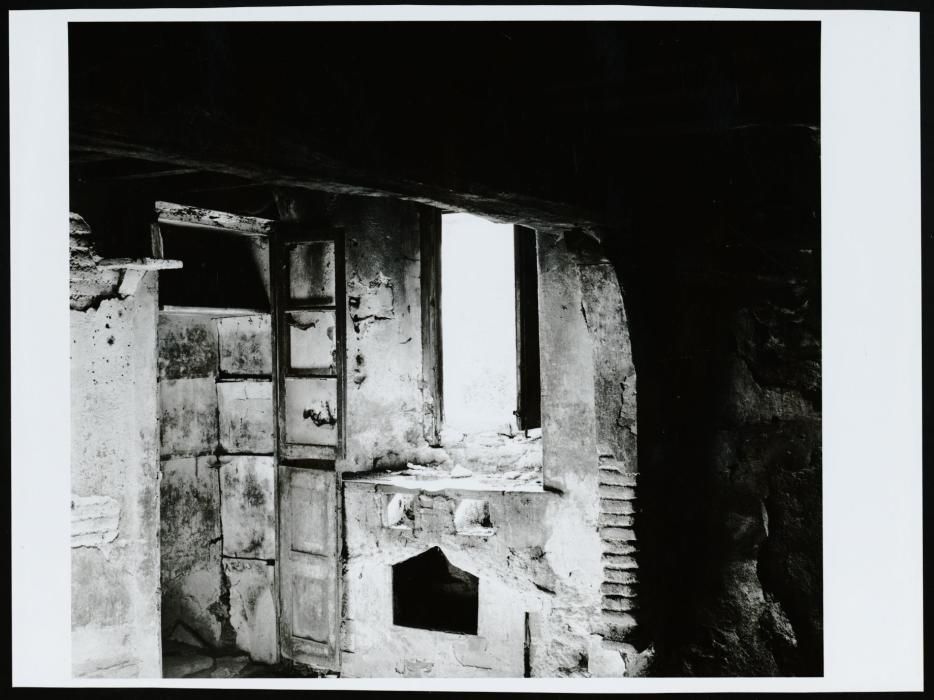 Fotografia d'un racó de la cuina d'una masia abandonada, hi trobem un armari encastat construït aprofitant una cantonada de la estança i una finestra sobre la cuina