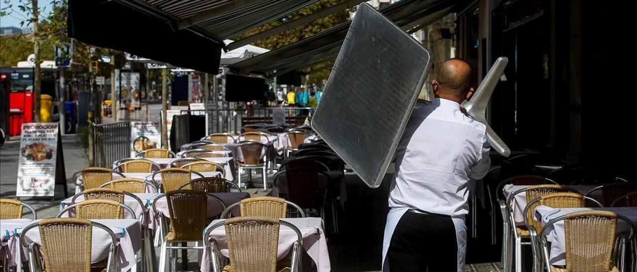 Un camarero recoge una mesa de una terraza de un restaurante del barrio de la Barceloneta.