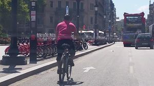 Un ciclista pedaleja pel centre de Barcelona amb una ampolla d’aigua sobre el cap
