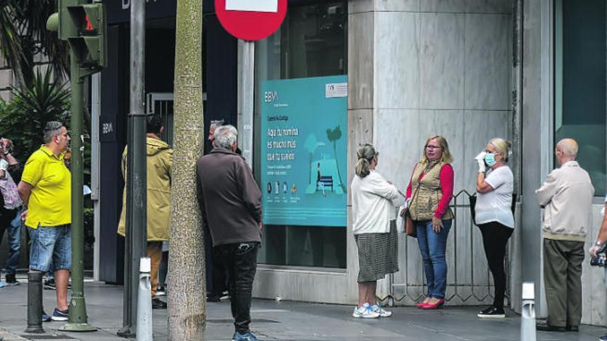 Un grupo de personas, alguna con mascarilla, aguarda en la entrada de una oficina bancaria de las Islas.