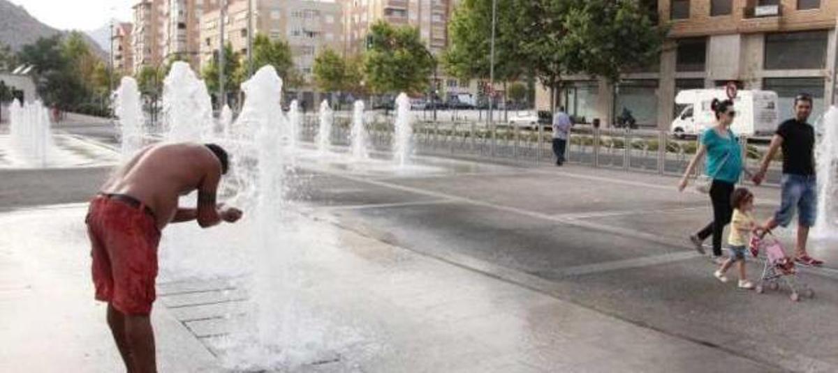 Un joven se refresca en una fuente en las calles de Elda.