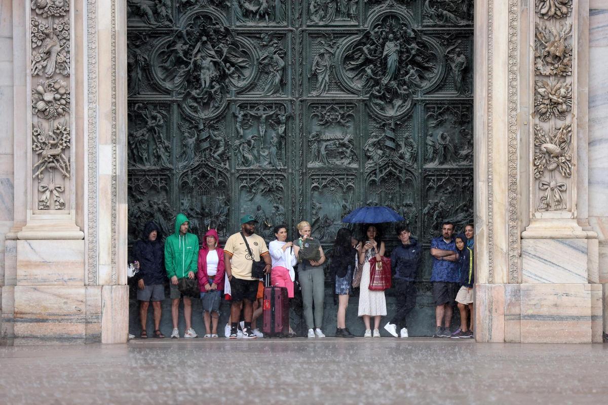 Un grupo de turistas se refugia de la lluvia en una de las puertas del Duomo de Milán.