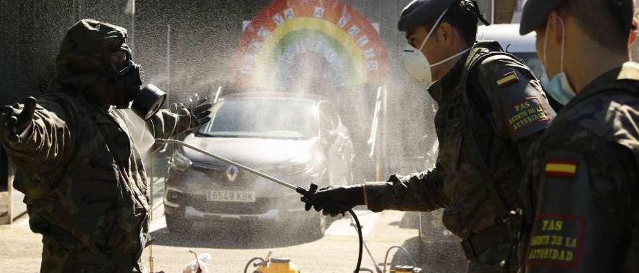Un militar desinfecta el uniforme de un compañero al finalizar unas tareas de higienización en Gijón.