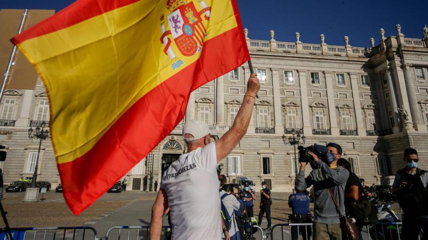 Un hombre ondea una bandera de España en el exterior del Palacio Real.