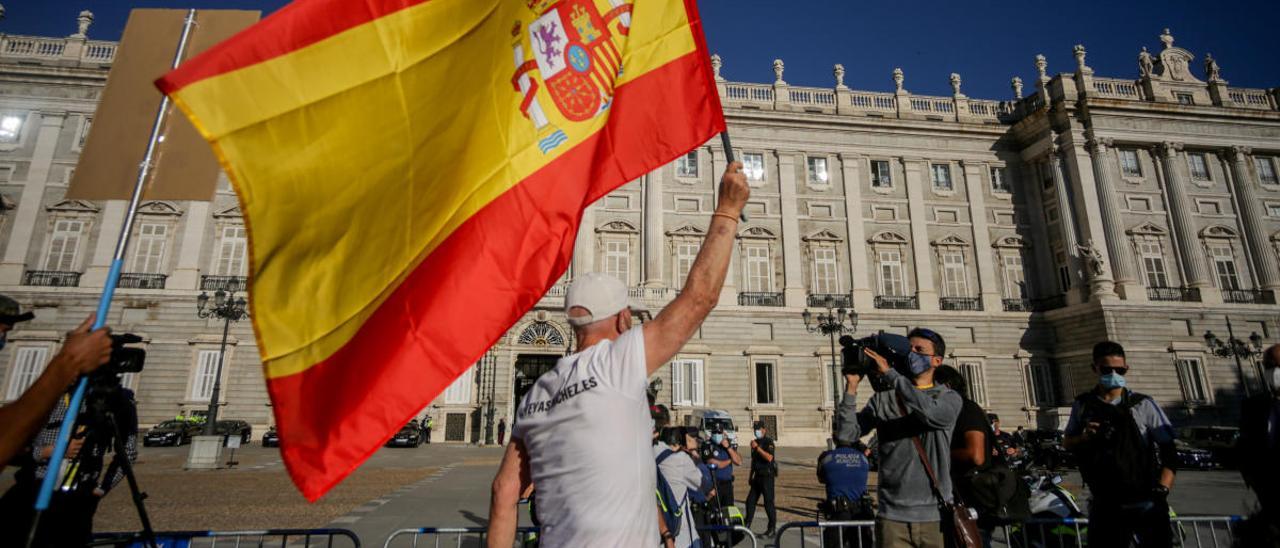 Un hombre ondea una bandera de España en el exterior del Palacio Real.