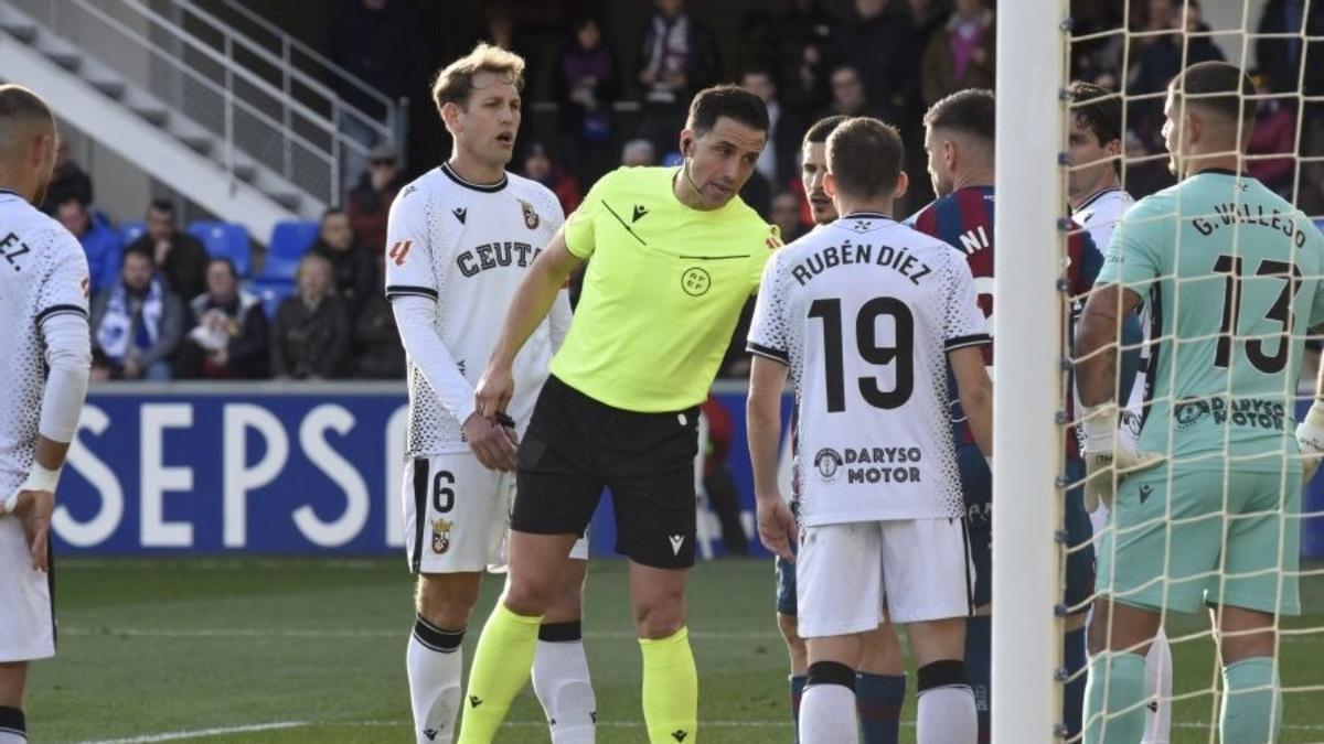 Ais Reig advierte a los jugadores del Ceuta y del Huesca antes de una jugada a balón parado.