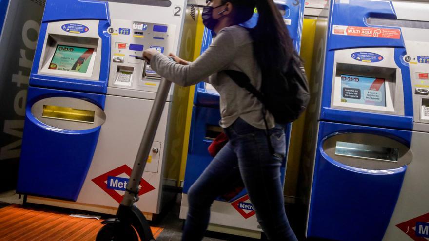 Archivo - Una mujer entra con un patinete eléctrico en el metro