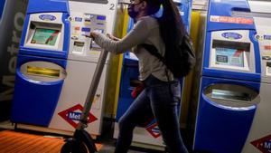 Archivo - Una mujer entra con un patinete eléctrico en el metro