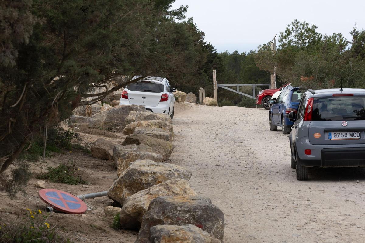 Vehículos aparcados en el camino cerrado con una barrera de hierro y, a la izquierda, una señal de prohibido aparcar en el suelo.