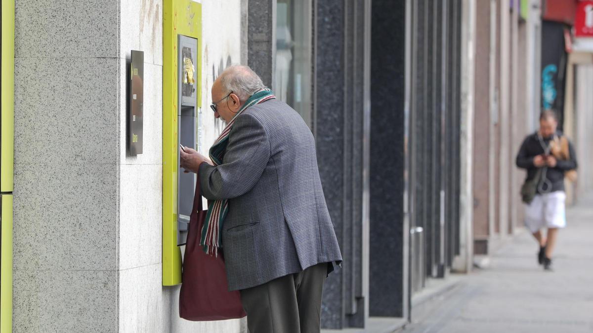 Una persona mayor saca dinero de un cajero en una calle.