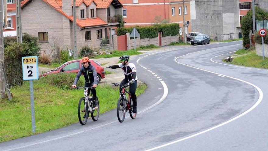 Dos ciclistas circulan por un tramo de la PO-313 donde se construirá el sendero peatonal. // Rafa Vázquez